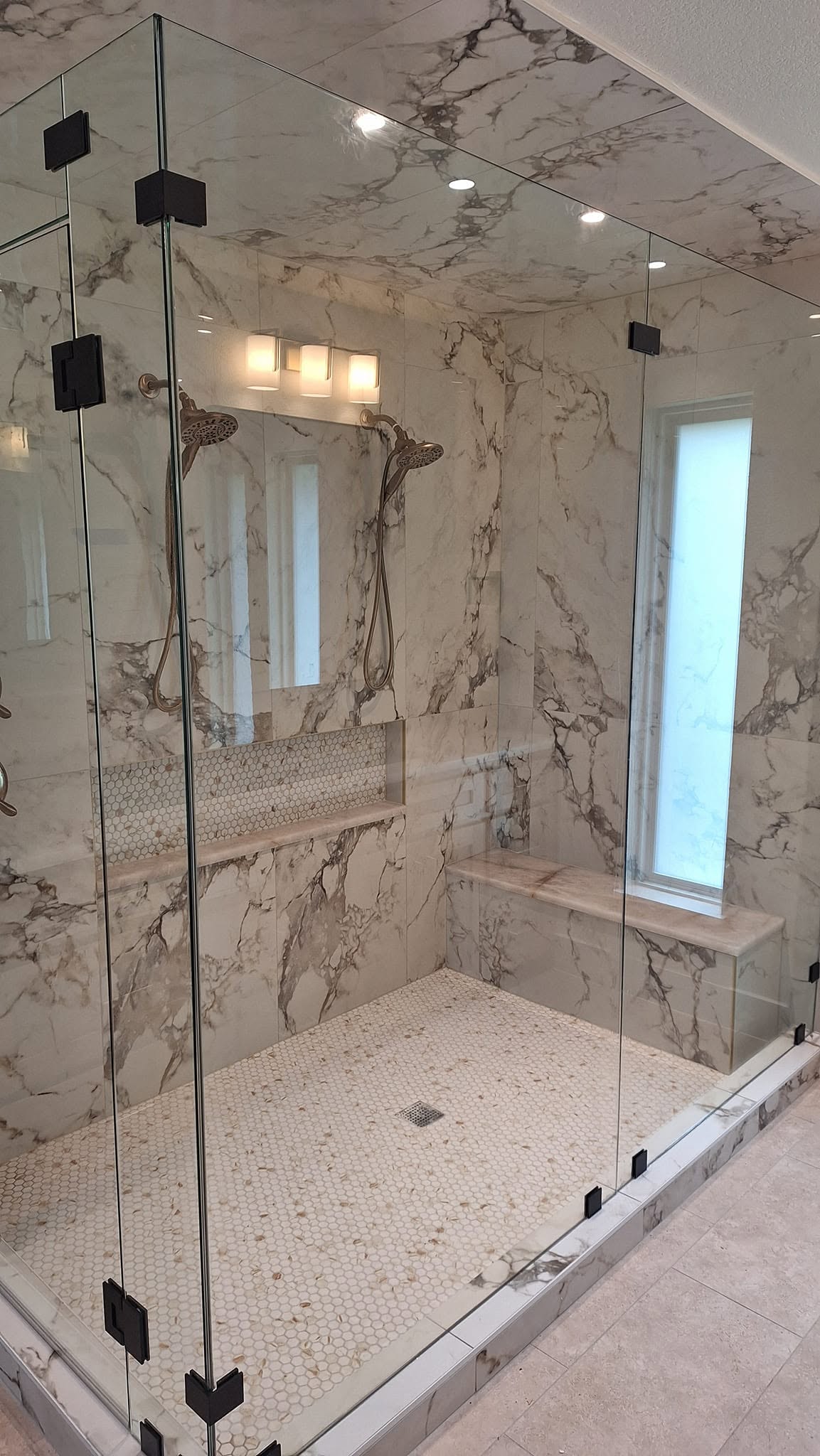 Large frameless shower enclosure with Calacatta tile and black hardware installed by Clearwater