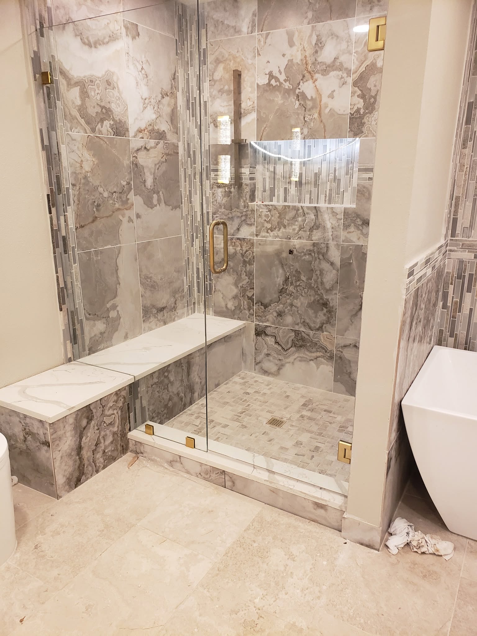 Frameless shower with stone tile and brushed brass hardware